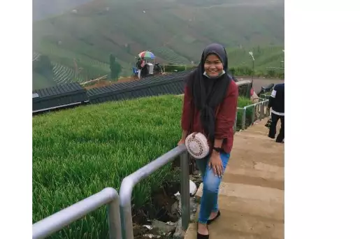 Seorang pengunjung berpose dengan latar belakang Terasering Panyaweuyan